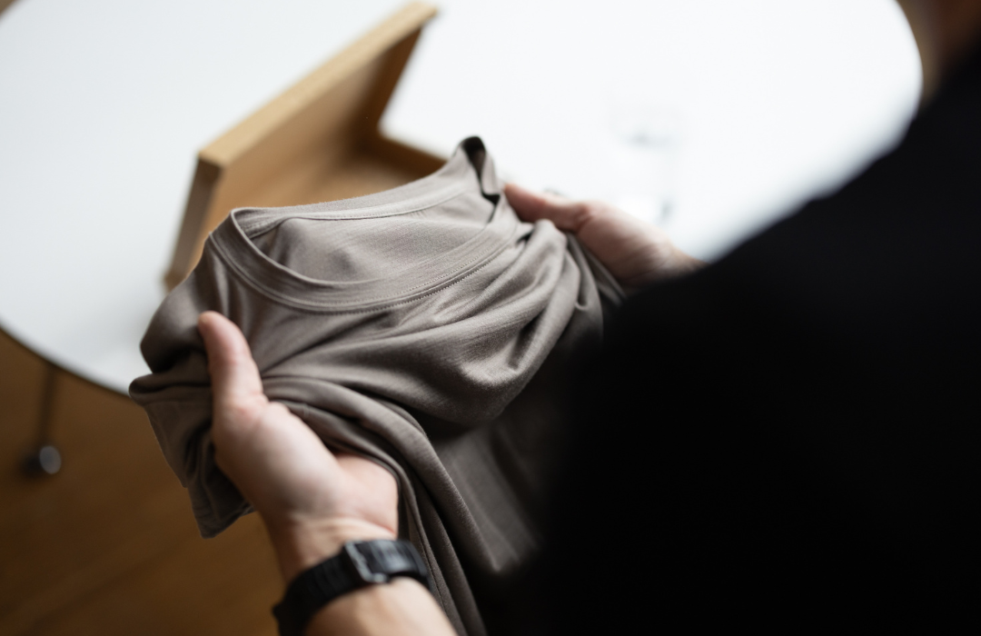 Hands holding a sand-colored LOOW merino T-shirt